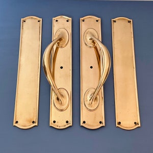 May include: Four gold-toned door handles with a decorative curved design. The handles are mounted on rectangular plates with rounded edges.