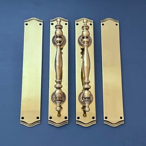 Puede incluir: Tres tiradores de puerta de latón con diseños ornamentados. Cada tirador tiene un pomo decorativo y una palanca larga y delgada. Los tiradores están montados en placas rectangulares con un borde decorativo.