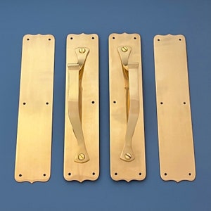 Pode incluir: Quatro puxadores de porta de latão com um design simples e elegante. Cada puxador tem uma forma retangular curva com a parte superior e inferior arredondadas. Os puxadores são polidos a um acabamento brilhante.