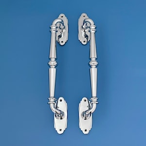 Peut inclure: Une paire de poignées de porte en chrome poli au design traditionnel. Les poignées ont une forme incurvée et un bouton décoratif en haut.
