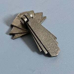 Pode incluir: Uma puxador de armário de metal prateado com um design geométrico art déco. O puxador tem uma base em forma de leque e uma pega longa e retangular.