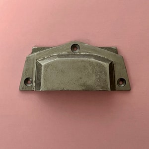 Può includere: Una maniglia per armadio in metallo argentato con un design geometrico. La maniglia ha una forma rettangolare con bordi arrotondati e un centro leggermente rialzato.