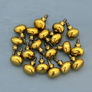 May include: A pile of 18 gold-toned cabinet knobs with a rounded shape and a screw on the back.