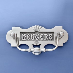 May include: Silver-toned metal door knocker with a decorative design and the word "LETTERS" engraved on the front.