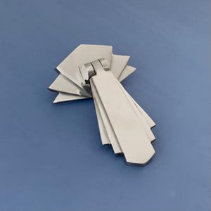 May include: A silver-toned, geometric cabinet pull with a fan-shaped design. The pull is made of metal and has a smooth, polished finish.