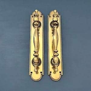 Puede incluir: Dos tiradores de puerta de latón ornamentados con un diseño decorativo. Los tiradores tienen un estilo tradicional y están hechos de latón pulido.