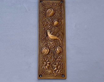 Puede incluir: Una placa de puerta rectangular de latón con un diseño ornamentado que presenta un pájaro, flores y granadas.