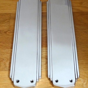 Pode incluir: Duas placas de porta prateadas com um design Art Deco. As placas são retangulares com bordas arredondadas e têm um acabamento liso e polido.