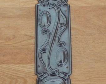 May include: A black metal door plate with an ornate design featuring a heart and floral motifs.