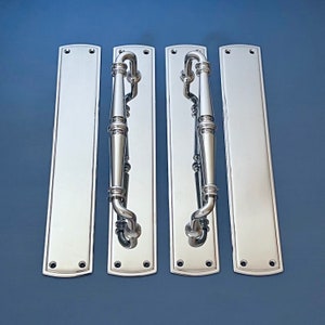 Puede incluir: Un juego de manijas de puerta cromadas pulidas y placas traseras rectangulares a juego. Las manijas tienen un diseño curvo con un agarre cilíndrico central. Las placas traseras son rectangulares con esquinas redondeadas.