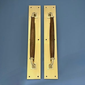 May include: Two gold door handles with wooden inserts. The handles are rectangular and have a simple design.