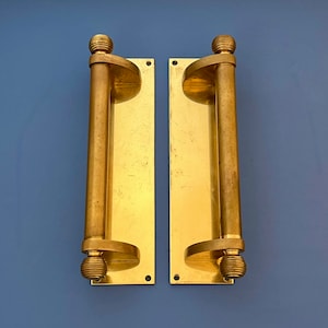 Può includere: Un paio di maniglie per porte in ottone antico con un design cilindrico. Le maniglie sono montate su piastre rettangolari con bordi arrotondati.