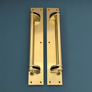 Puede incluir: Un par de manillas de puerta de latón pulido con un diseño simple y elegante. Cada manilla tiene una empuñadura cilíndrica curva y una placa posterior rectangular.