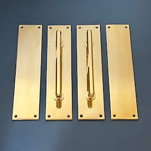 May include: Four gold-colored door pulls with a rectangular plate and a long, cylindrical handle. The plates have rounded corners and two small holes on each side.