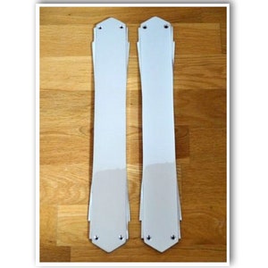 Puede incluir: Dos tiradores de puerta de metal blanco con un diseño decorativo. Los tiradores están montados en una superficie de madera.