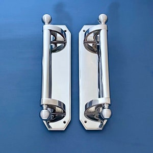 May include: A pair of polished chrome door handles with a decorative design. Each handle has a round knob at the top and bottom.