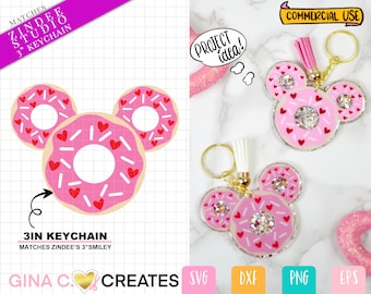 Op de afbeelding: Een roze en witte donut sleutelhanger met rode hartjes en witte sprinkles. De donut is gevormd als Mickey Mouse's hoofd. De sleutelhanger is gemaakt van hars en heeft een diameter van 7,6 cm. De tekst "MATCHES ZINDEE'S 3"SMILEY" staat onderaan de afbeelding.