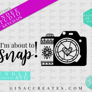 May include: Black and white graphic of a camera with the text "I'm about to snap!" and "Zindee Studio 3" Keychain". The camera design includes a floral element and a heart shape in the lens.