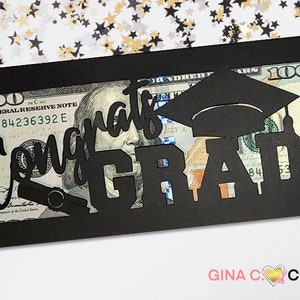 May include: Black cardstock money holder with a cut-out design that says "Congrats Grad!" with a graduation cap and a diploma. A $100 bill is visible through the cut-out.