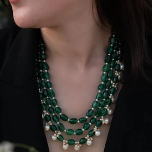 Peut inclure: Collier à plusieurs rangs avec des perles vertes ovales et de petites perles blanches. Le collier a un design classique. Les perles sont d'un vert émeraude profond et les perles ajoutent une touche d'élégance.