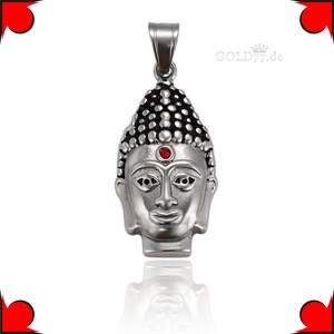 Puede incluir: Colgante de plata con una cabeza de Buda detallada con una piedra preciosa roja en el centro de la frente. El colgante tiene un dise&ntilde;o texturizado en negro y plata.
