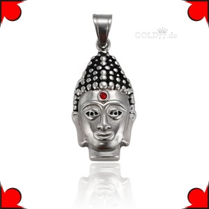 Puede incluir: Colgante de plata con una cabeza de Buda detallada con una piedra preciosa roja en el centro de la frente. El colgante tiene un dise&ntilde;o texturizado en negro y plata.