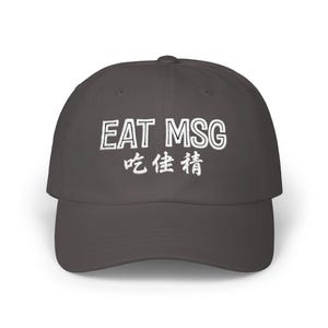 May include: A dark gray baseball cap with the embroidered text "EAT MSG" in white, above Chinese characters. The cap has a curved brim and a structured crown, suitable for casual wear.
