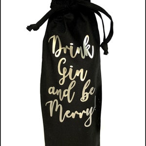 Könnte beinhalten: Schwarze Stofftasche für eine Weinflasche mit einem silbernen Metallic-Design, auf dem "Drink Gin and Be Merry!" steht.