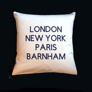 Può includere: Cuscino bianco con testo blu scuro che recita "LONDON NEW YORK PARIS BARNHAM"