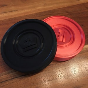 May include: Two round game pieces, one black and one red. The black piece has a crown design in the center. The red piece has a star design in the center.