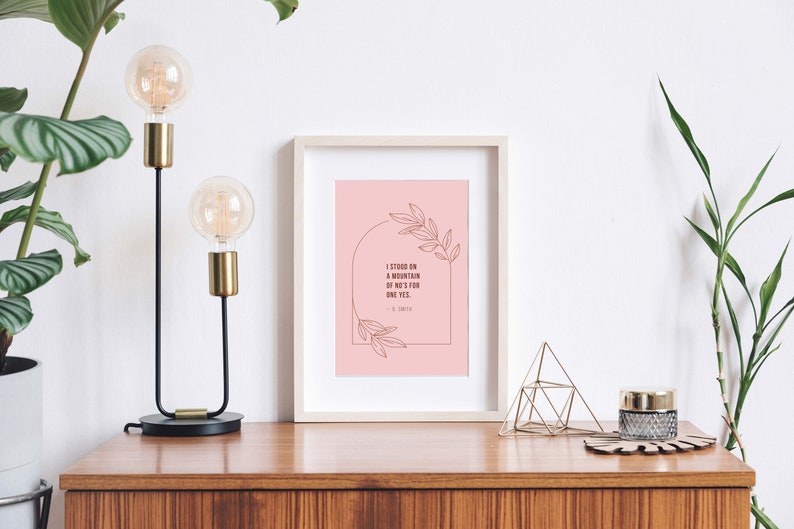 May include: A framed print with a pink background and a quote in brown text that reads "I stood on a mountain of no's for one yes." The quote is surrounded by a line drawing of leaves and a half circle.