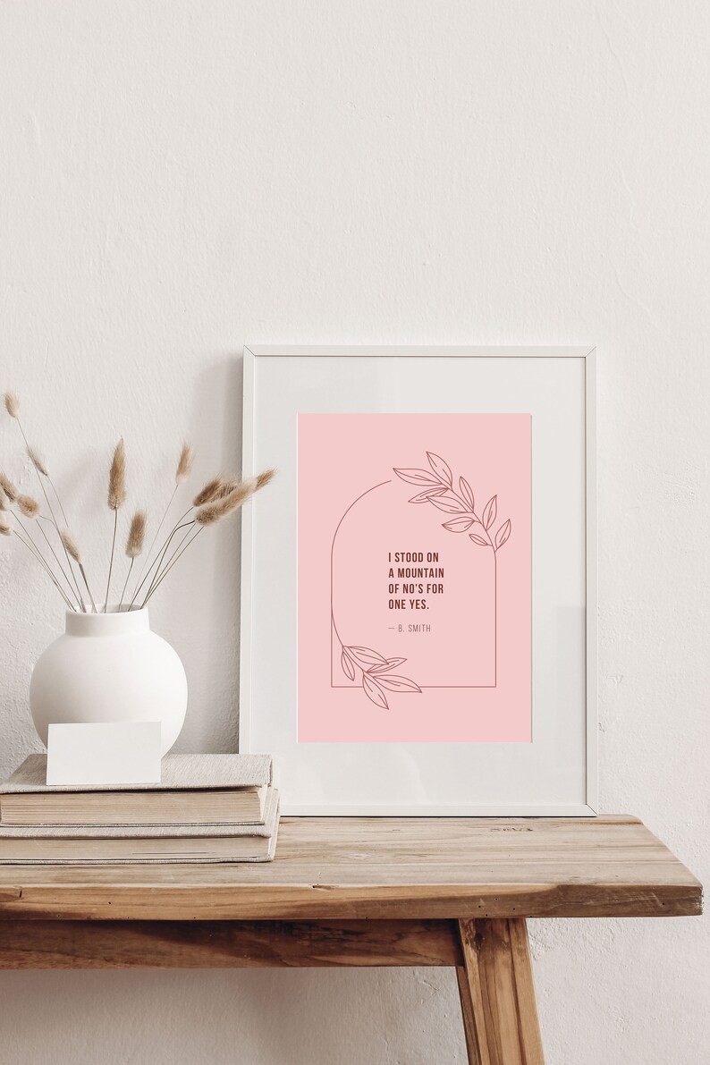 May include: A white framed print with a pink background and a quote that reads "I stood on a mountain of no's for one yes. - B. Smith" with a floral design around the quote.