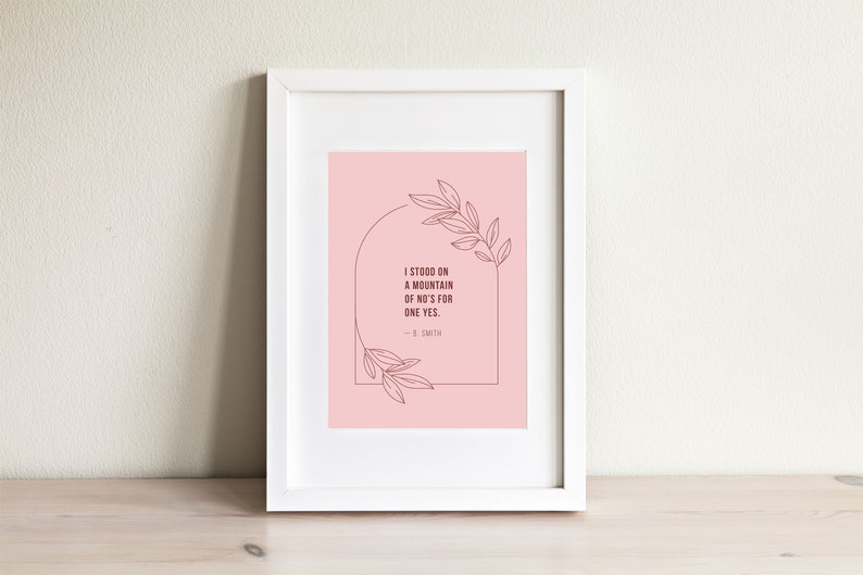 May include: A framed print with a pink background and a quote that reads "I stood on a mountain of no's for one yes. -  E. Smith". The quote is surrounded by a line drawing of a leafy branch.