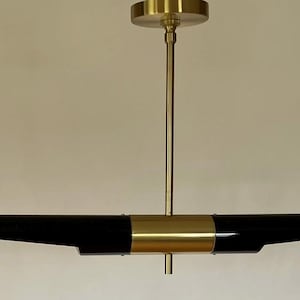 May include: A contemporary pendant light, featuring a black, horizontal body with gold detailing. The central section is a gold band, and the light is suspended from a gold ceiling fitting. The overall length is approximately 90 cm.