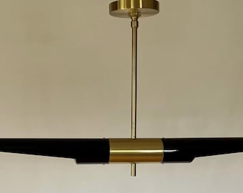 Könnte beinhalten: Moderne Pendelleuchte in Schwarz und Gold. Der horizontale schwarze Korpus hat goldfarbene Akzente und ein zentrales goldenes Band. Sie wird von einer goldfarbenen Deckenhalterung abgehängt. Ca. 90 cm lang.