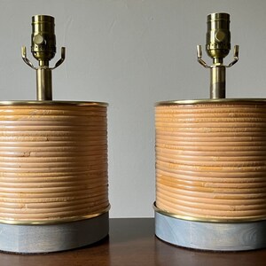 May include: A pair of table lamps with a woven bamboo base and a brass lampshade. The bases are painted a light gray color.