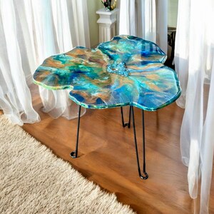 May include: A blue, green, and gold resin table top with a unique, organic shape. The table has a black metal hairpin leg base.