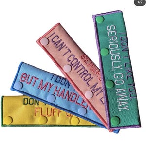 May include: Four colourful fabric straps with embroidered text and snap buttons. The straps read "Don't like you seriously go away", "Beware I can't control my", "I don't handle fluff", and "But my handle".