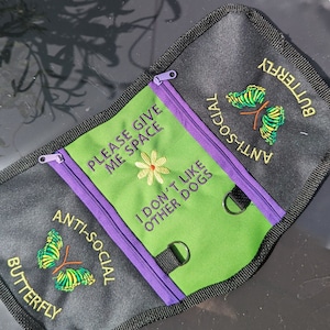 Peut inclure: Une pochette zippée noire avec un panneau vert sur lequel est inscrit le texte "Please give me space" et "I don't like other dogs". La pochette présente également un motif de papillon avec le texte "Anti-social butterfly" des deux côtés.