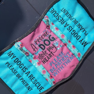 May include: A pink and blue fabric pouch with a zipper closure. The pouch has the text "My dog is a rescue, please be patient" on the front and "A rescue dog stole my heart, please be patient with them" on the back.