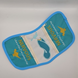 Könnte beinhalten: Eine türkisblaue Reißverschlusstasche mit weißem Stoff und goldener Stickerei. Die Tasche hat zwei Fächer und der Text "NERVOUS Like a star I've come so far" ist auf der Vorderseite gestickt.