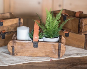 May include: Three wooden boxes with leather handles and metal accents. The center box is filled with a white candle, a small green plant, and a larger green fern plant in a white pot.