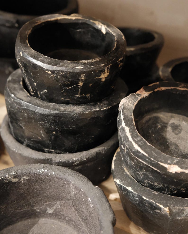 May include: A stack of several black, round, wooden bowls with a distressed finish. The bowls have a dark, matte appearance with visible wear and tear, and some areas of exposed wood.