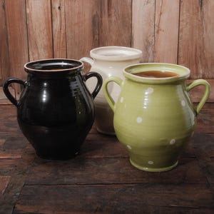 May include: Three ceramic crocks with different colored glazes. The crock on the left is black, the middle crock is white, and the crock on the right is green with white polka dots.