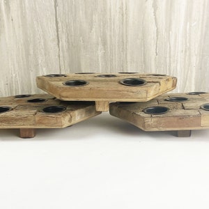 May include: A set of three wooden candle holders, each with a hexagonal shape and multiple candle slots. The holders are stacked on top of each other, creating a tiered display.