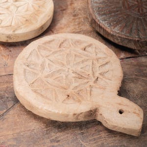 May include: A collection of hand-carved wooden objects with intricate geometric patterns. The objects are various sizes and shapes, including round and oval forms. The wood has a natural, light brown color, and the carvings create a textured surface.