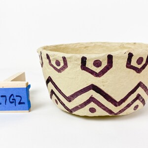 K&ouml;nnte beinhalten: Eine kleine, cremefarbene Schale mit einem geometrischen Muster aus braunen Zickzacklinien und Punkten. Die Schale ist aus Papiermach&eacute; gefertigt und hat eine raue Textur.