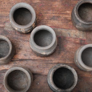 Peut inclure: Vue a&eacute;rienne de sept petits pots en c&eacute;ramique grise, us&eacute;s, avec de larges ouvertures. Les pots sont dispos&eacute;s sur une surface en bois rustique et sombre. Ils pr&eacute;sentent une texture rugueuse et des signes d'&acirc;ge.