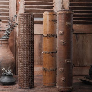 May include: Three tall, cylindrical containers made of wood with intricate carvings and patterns. The containers are brown and have a rustic appearance. They are standing on a wooden floor.