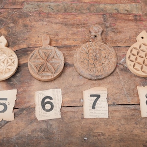 May include: Four round, wooden, decorative cutting boards with carved floral and geometric designs. Each board has a handle. Below the boards are four torn pieces of paper with the numbers 5, 6, 7, and 8 printed on them.
